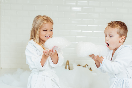 adorable little kids in bathrobes playing with foam in bathroom
