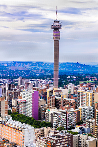 Johannesburg portrait cityscape in the afternoon across Hillbrow residential suburb of towering apartments. The iconic Hillbrow communication tower seen on the left. Johannesburg is one of the forty largest metropolitan cities in the world, and the world's largest city that is not situated on a river, lakeside, or coastline. It is also the source of a large-scale gold and diamond trade, due being situated in the mineral-rich Gauteng province.