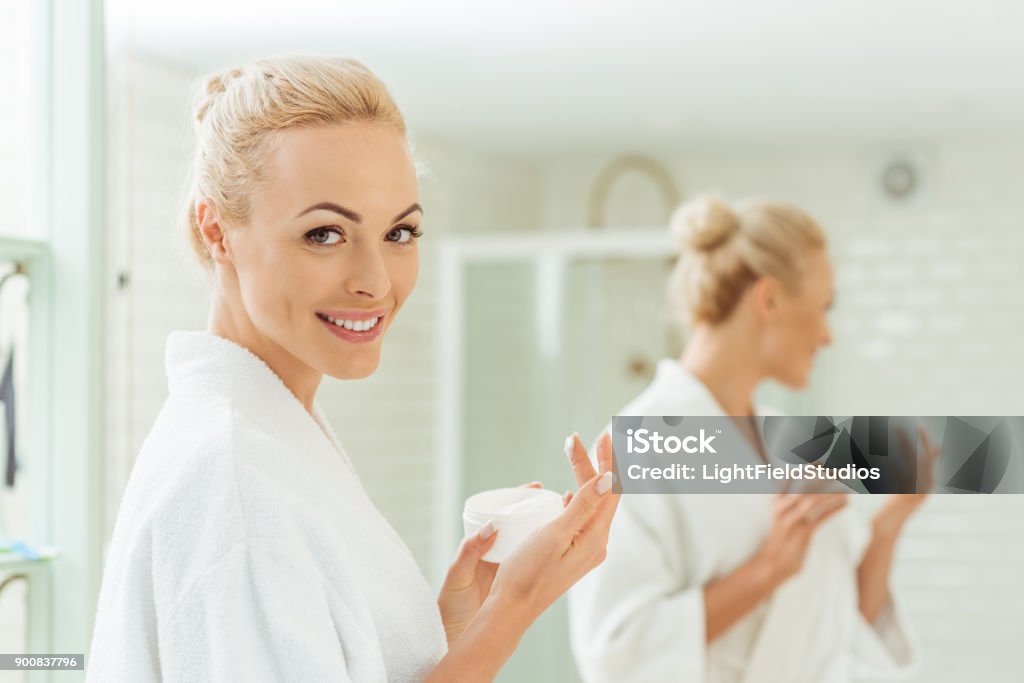 donna in accappatoio applicando crema viso - Foto stock royalty-free di Crema viso