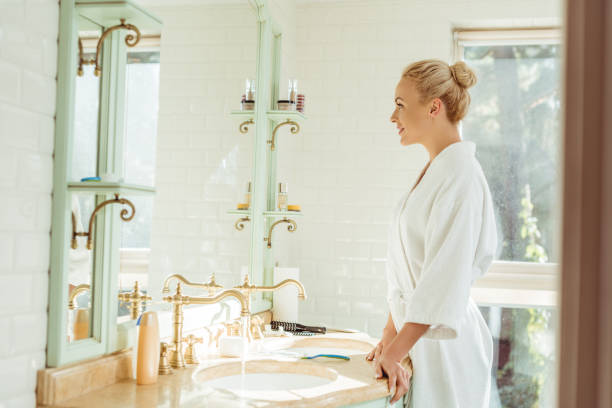 istock woman in bathrobe looking at mirror 900840024