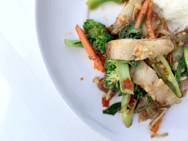 istock Stir Fried Crispy pork with Roasted Chili Paste and mixed vegetables;  basil; kale; broccoli; carrot; red chilli & Fried egg with Thai jasmine rice in white dish on white background. Thai style food. 900840252