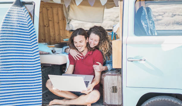 happy couple using laptop computer in road trip vacation - travel couple having fun watching videos inside minivan - love, van lifestyle, surf and relationship concept - focus on faces - hipster people surfing the net internet imagens e fotografias de stock