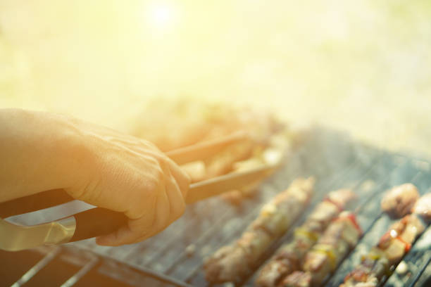 バーベキューで肉を調理する若者 - シェフは、公園の屋外でグリルにいくつかの肉串を置く - 夏の間に屋外で食べるという概念 - トップハンドにソフトフォーカス - ヴィンテージレトロなフ� - barbecue grill chef barbecue sausage ストックフォトと画像