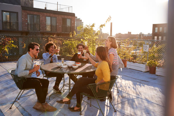 fünf freunde sitzen an einem tisch auf einem dach machen einen toast - freunde imbiss großstadt stock-fotos und bilder