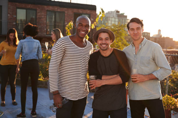 istock Three male friends at a rooftop party smiling to camera 900855630