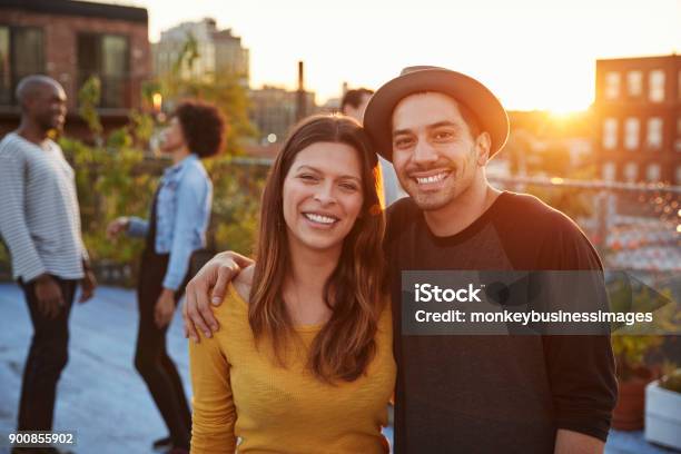 Young Adult Couple Embracing At A Rooftop Party Stock Photo - Download Image Now - Couple - Relationship, Latin American and Hispanic Ethnicity, Friendship