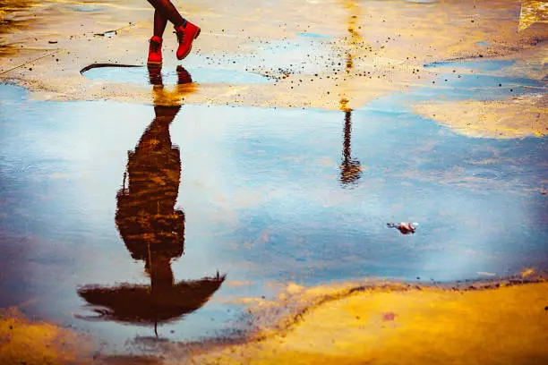 Photo of Reflection in a puddle of a young woman holding umbrella, on a cold, windy, rainy autumn day.