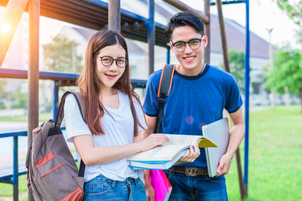 istock Two Asian young college people discussing about reading book and using laptop for search and learn knowledge. Education and Friendship concept. Happiness and Learning concept. Lovers and Friend theme. 900875318
