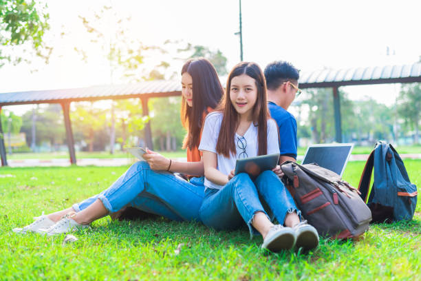 istock Group of Asian college student using tablet and laptop on grass field at outdoors. Technology and Education learning concept. Future Technology and Modern entertainment concept. Edutainment theme. 900875328