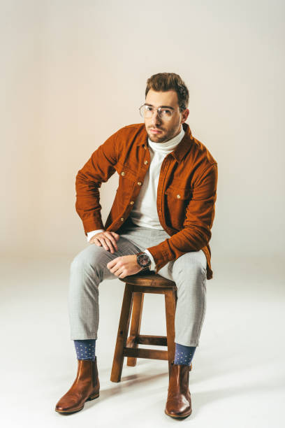 istock stylish man looking at camera while sitting on wooden chair, on beige 900883312