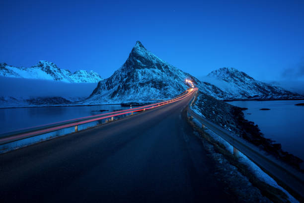 Olstind Mount and car light. Lofoten islands, spring time, Norway Olstind Mount and car light. Lofoten islands, spring time, Norway winter sunrise mountain snow stock pictures, royalty-free photos & images