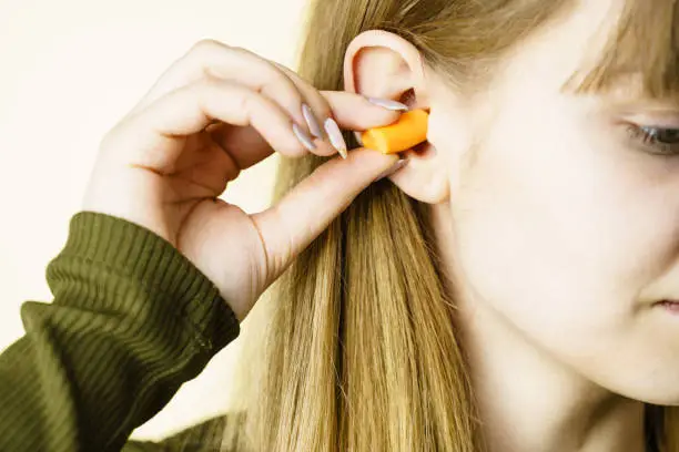 Woman putting ear plugs into her ears getting rid on noise in loud place.