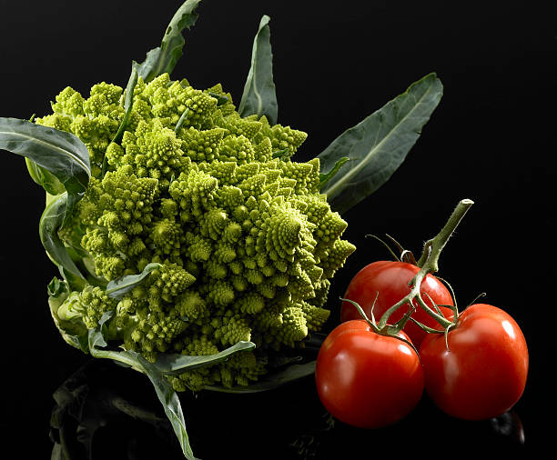 romanesco cauliflower and tomatoes studio shot of a romanesco cauliflower and 3 Tomatoes in black reflective back vermehrung stock pictures, royalty-free photos & images