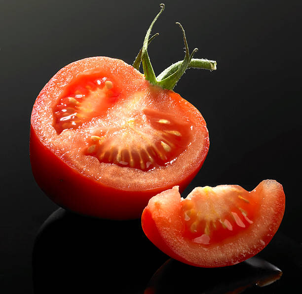 tomato and cut half tomato and cut in black reflective back vermehrung stock pictures, royalty-free photos & images