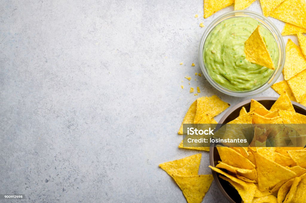 Traditional mexican homemade guacamole sauce in a glass bowl and Traditional mexican homemade guacamole sauce in a glass bowl and a bowl with tortilla chips on a light stone background. Party food concept.  Top view, copy space, horizontal image Tortilla Chip Stock Photo