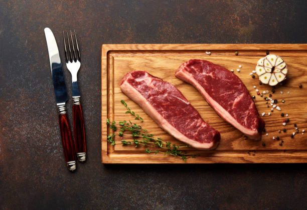 新鮮な生肉 picanha ステーキ、伝統的なブラジルは、木の板にローズマリー、ニンニク、ナイフ、黒胡椒をカットしました。スライスした肉のステーキ。平面図です。 - picanha beef meat rare ストックフォトと画像