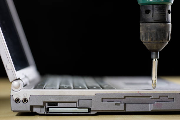 A laptop on a wooden table seen from the profile together with carpentry tools. Computer repair in a workshop. Black background.