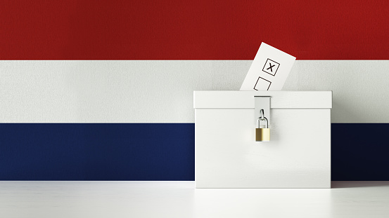 Dutch presidential and legislative elections concept. A vote envelope is entering into a ballot box. Ballot box is in front of a waving Dutch flag and it is made of wood. Horizontal composition with copy space. Great use for referendum and elections related concepts.
