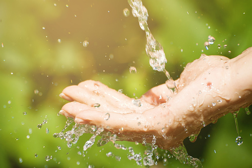 Woman washing hand outdoors. Natural drinking water in the palm. Young hands with water splash, selective focus