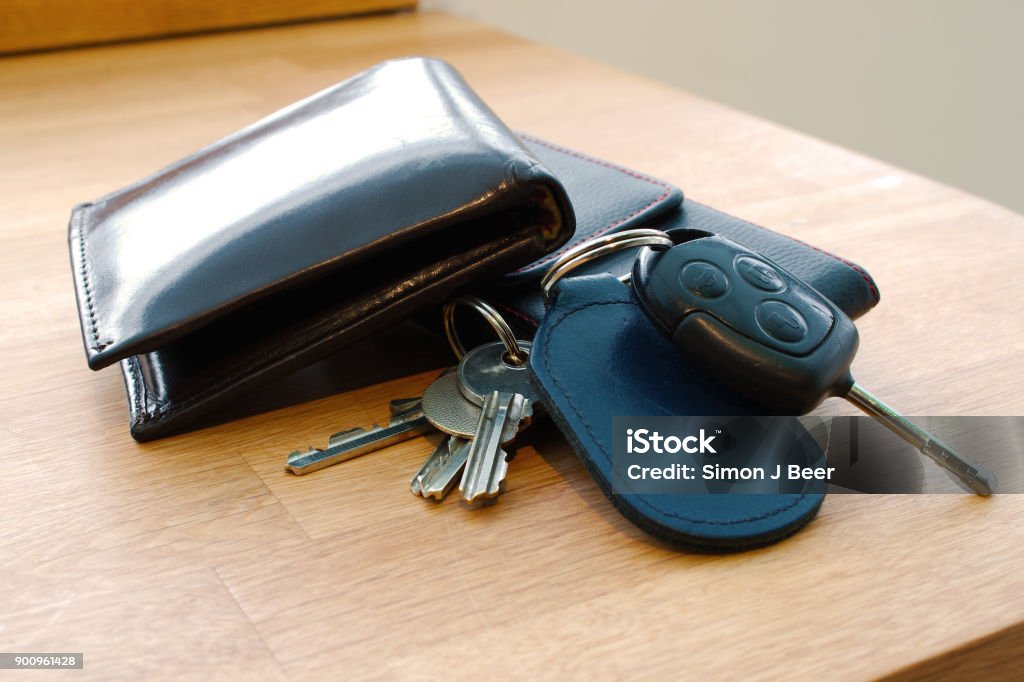 Wallet, car key, house keys and mobile phone on a table. Wallet, car key, house keys and mobile phone on a table together in such a way that looks like someone is about to leave or has just arrived. Photographed; Barnstaple, Devon, UK. December 2017 Wallet Stock Photo