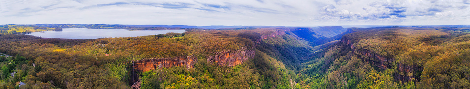 Wide aerial panorama of MOrton National park from Fitzroy lake with tall waterfall falling down to Yarrunga valley creek of gum-tree covered cliffs and mountains.