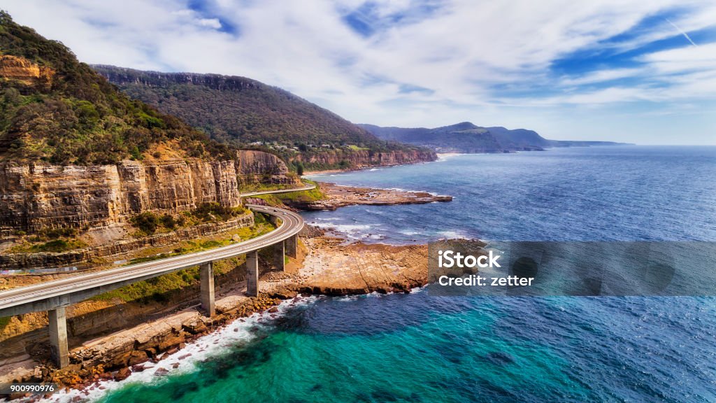 D Sea Cliff Bridge 2 Norh Side Aerial view of famous Sea Cliff Bridge on Grand Pacific drive in NSW, Australia. Scenic highway on the edge of sandstone cliff over tiding surfing waves of open Pacific ocean on a sunny day. Australia Stock Photo