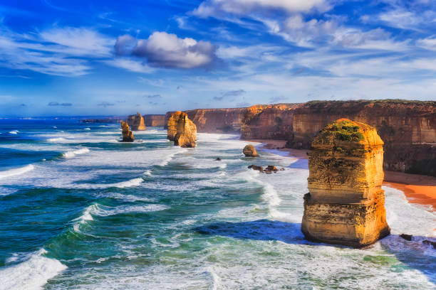 GOR 7 apostles day Disconnected eroded limestone rocks of twelve apostles rock formation in marina park on the Great Ocean road during day time in bright sunlight under cloudy blue sky. twelve apostles sea rocks victoria australia stock pictures, royalty-free photos & images