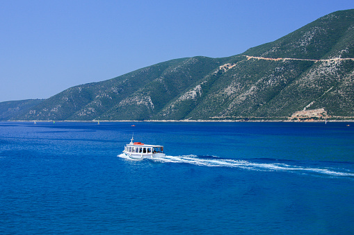 A small passenger boat travelling on the deep blue sea of Mediterana with some white trails behind