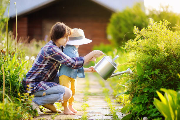 schöne frauen und ihren süßen enkel bewässerung von pflanzen im garten am sonnigen sommertag - baby toddler child flower stock-fotos und bilder