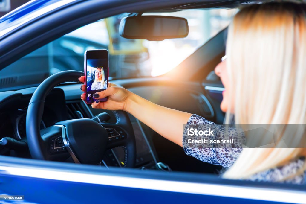 Young woman driver taking a selfie in her car Young happy smiling woman driver taking a selfie photo on a smartphone in her modern luxury car Selfie Stock Photo
