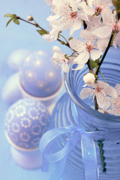 istock Easter eggs in egg cups with cherry blossoms in glass vase on blue 901002130