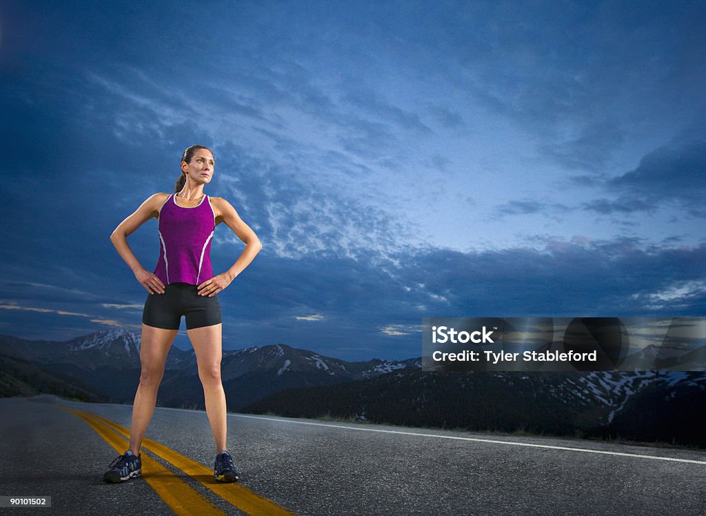 A female runner stands confidently on a road. The runner is surrounded by mountains near Independence Pass outside of Aspen. Front View Stock Photo