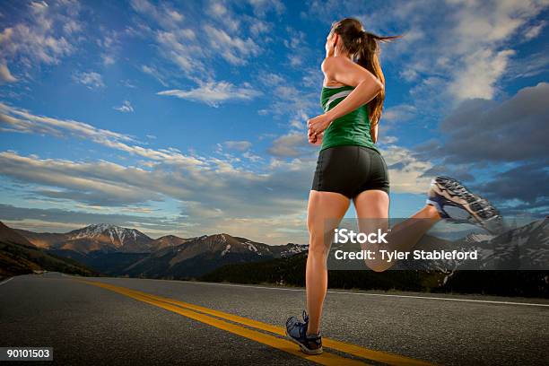 A Female Athlete Runs Down A Road In The Mountains Stock Photo - Download Image Now - Running, One Woman Only, Rear View
