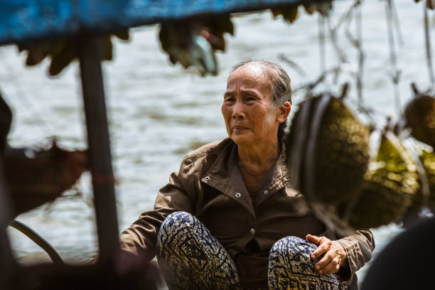 My Tho, Vietnam - January 04, 2016: an old vietnamese woman crouching on a wodden boat selling fruits on the Mekong river in My Tho, Vietnam.
