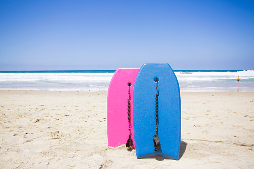 Two colorful boogie boards resting on a pristine beach. Ready to ride and have fun in the ocean on a clear summer day. Vacation time