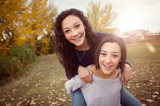 Hispanic Teenage girls having fun together outdoors Cute hispanic teenage girls playing together outdoors during a warm fall day. Sun flare in the background sibling stock pictures, royalty-free photos & images