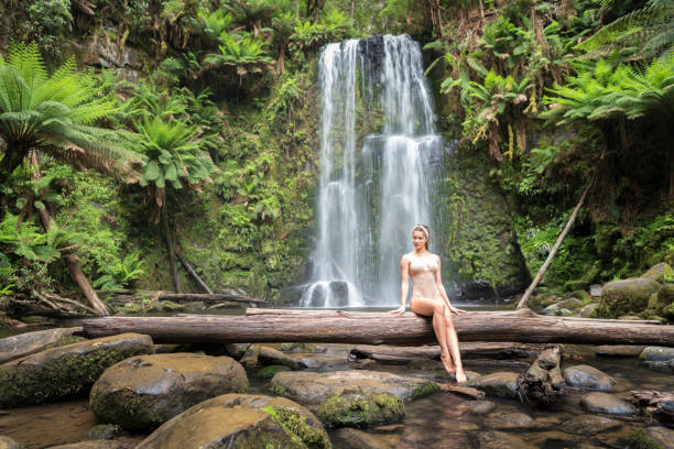 piękna kobieta siedząca na logu przed oszałamiającym wodospadem, powrót do natury, wodospad beauchamp, great ocean road - rainforest forest river australia zdjęcia i obrazy z banku zdjęć