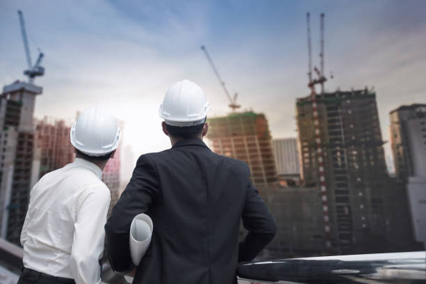 istock Asian businessman looking and point to finger away and engineer architect hold construction industrial plan background for working together as team concept, back view 901060564