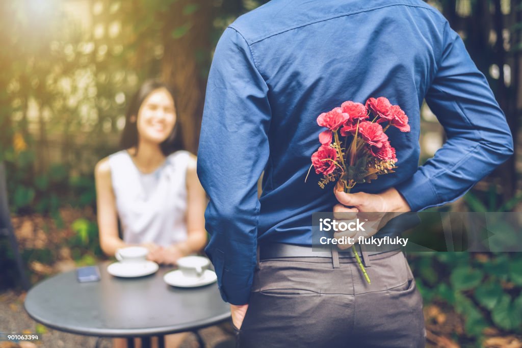 The man is hiding red flowers behind him in order to surprise his girlfriend. Dating Stock Photo