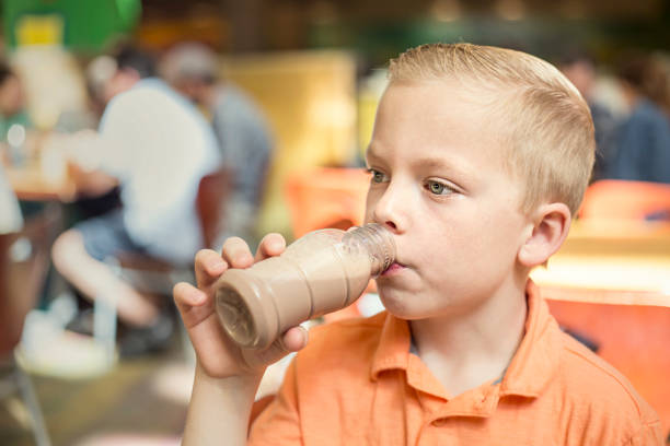 Cute boy drinking a bottle of chocolate milk during school lunch at his elementary school cafeteria. Healthy eating habits being taught at the public school system