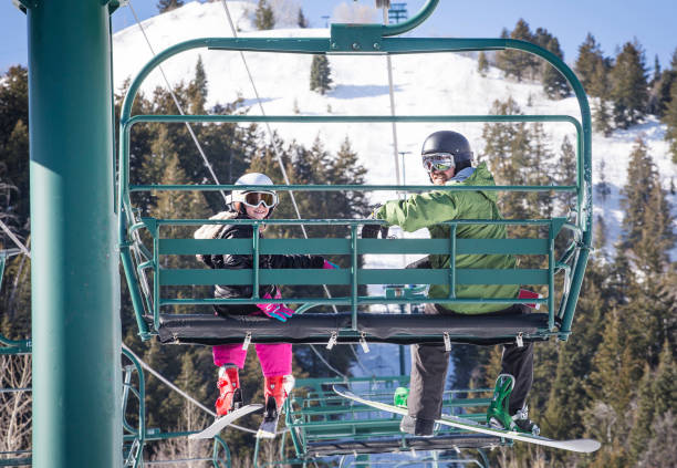 Father and daughter riding a chair lift together at a ski resort Smiling father and daughter riding a chair lift together on a sunny day at a ski resort ski lift photos stock pictures, royalty-free photos & images