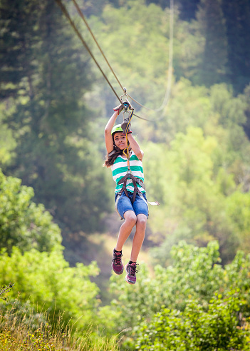 Happy diverse little girl riding a zip line in a lush mountain forest while on family vacation