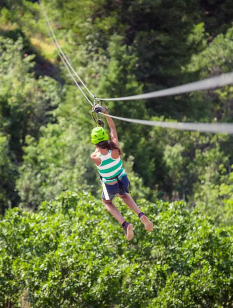 Diverse Teen girl riding a zip line in a lush mountain forest while on vacation. View from behind. Lots of copyspace