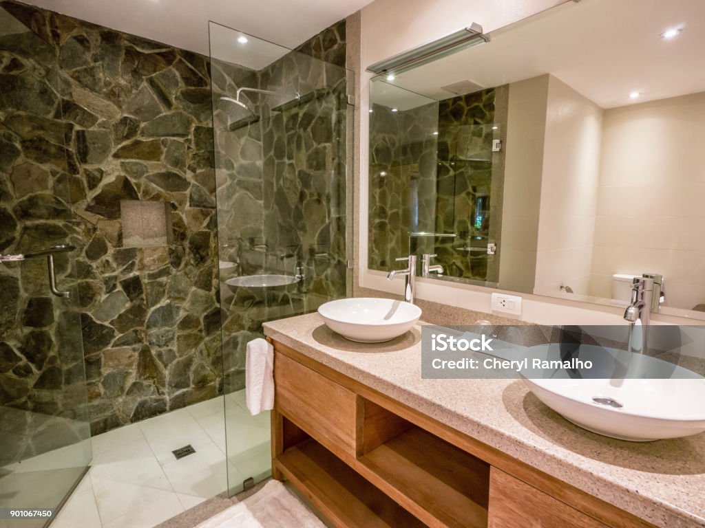 Modern bathroom with two round, white vessel sinks on granite counter. Natural stone and glass shower enclosure. Generic bathroom with double ceramic sinks on and single-hole chrome faucets on granite counter tops. Glass and stone shower. Bathroom Stock Photo