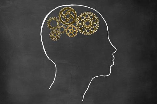 Close-up of human head with metal gears drawn on the blackboard.