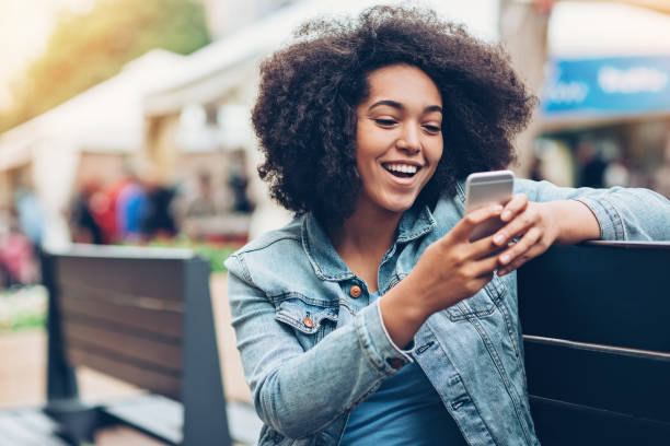 Checking what's on social media Young African ethnicity woman sitting on a bench and texting denim jacket stock pictures, royalty-free photos & images