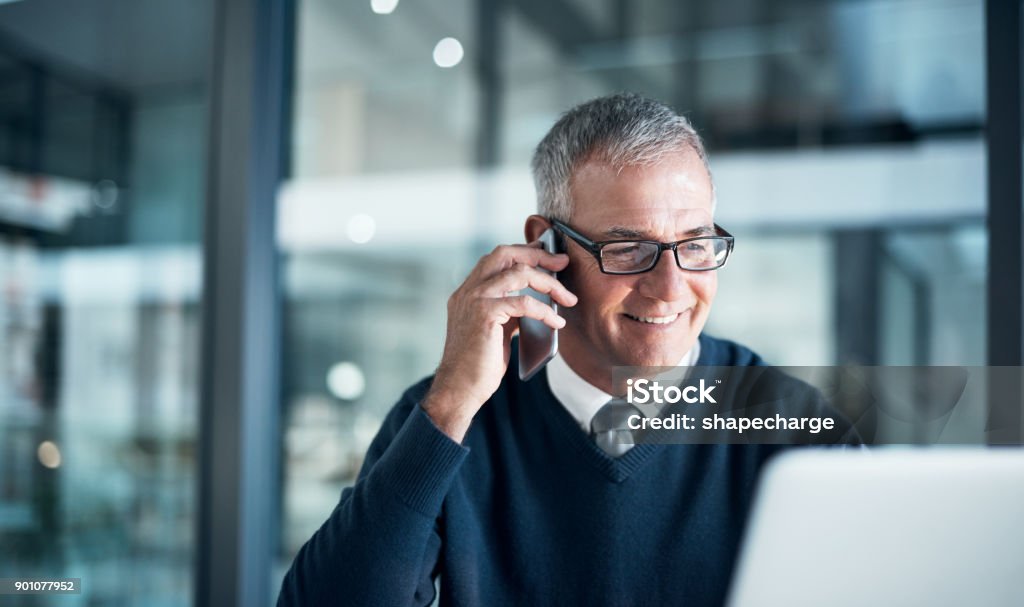 What career dedication looks like Shot of a mature businessman using a cellphone and laptop while working late in an office Senior Adult Stock Photo