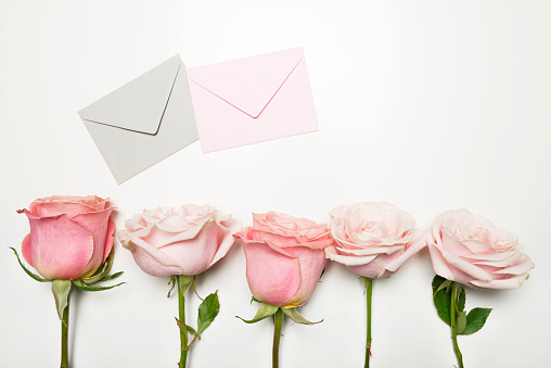 Two envelopes and five roses in a row on white table.