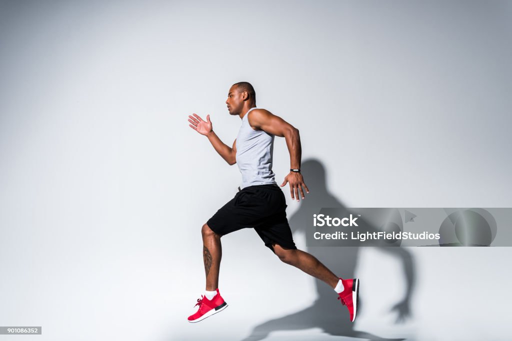 sportsman running on grey side view of young african american sportsman running on grey Activity Stock Photo