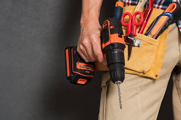 Hand holding construction tools Close up of handyman holding a drill machine with tool belt around waist. Detail of artisan hand holding electric drill with tools isolated over grey background. Closeup hand of bricklayer holding carpentry accessories. screwdriver stock pictures, royalty-free photos & images